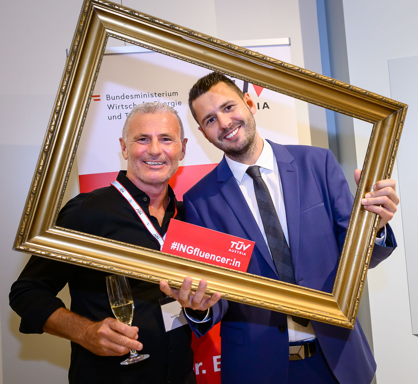 <br /> Zwei freundlich lächelnde Herren schauen durch einen leeren Bilderrahmen.